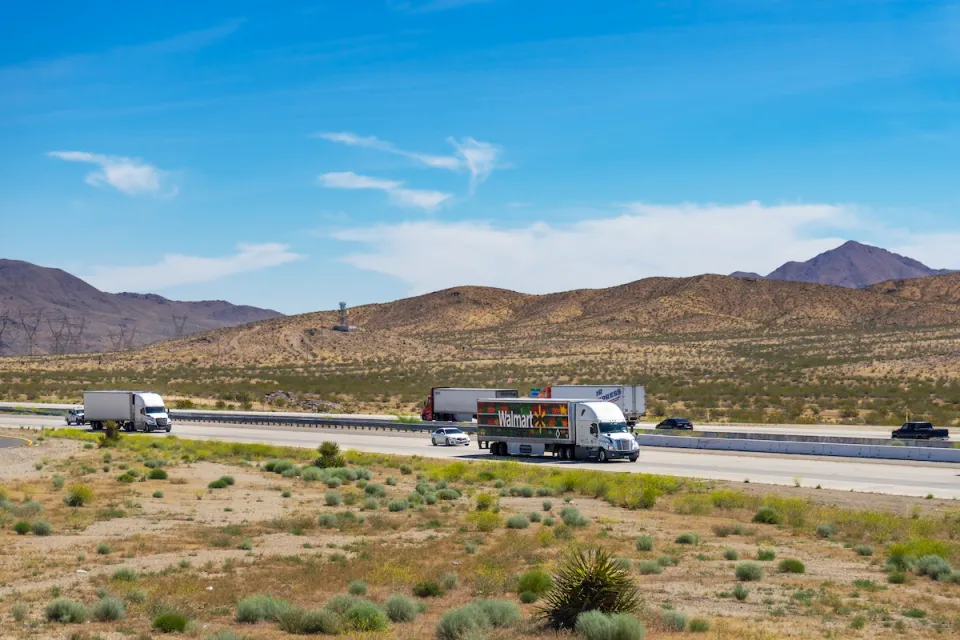 View of trucks on Interstate 15 with desert mountains in background in Southern California.